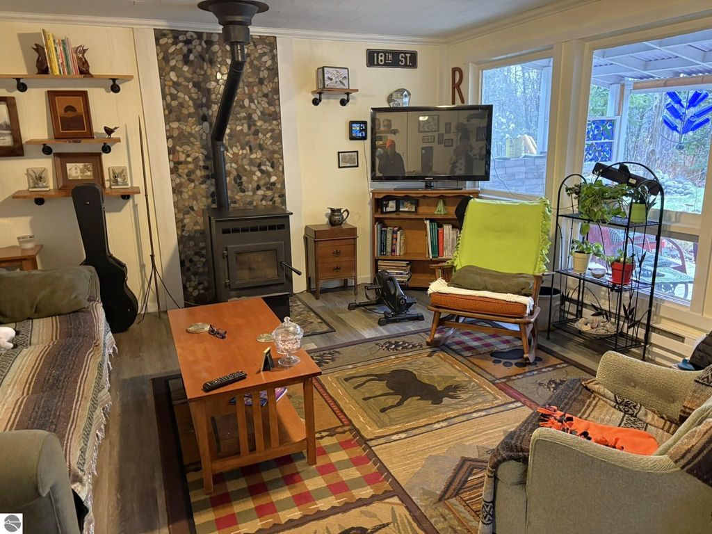 Cozy living room interior of a waterfront cottage in Grawn, MI, featuring a pellet stove, wooden furniture, decorative rugs, and large windows with natural light.