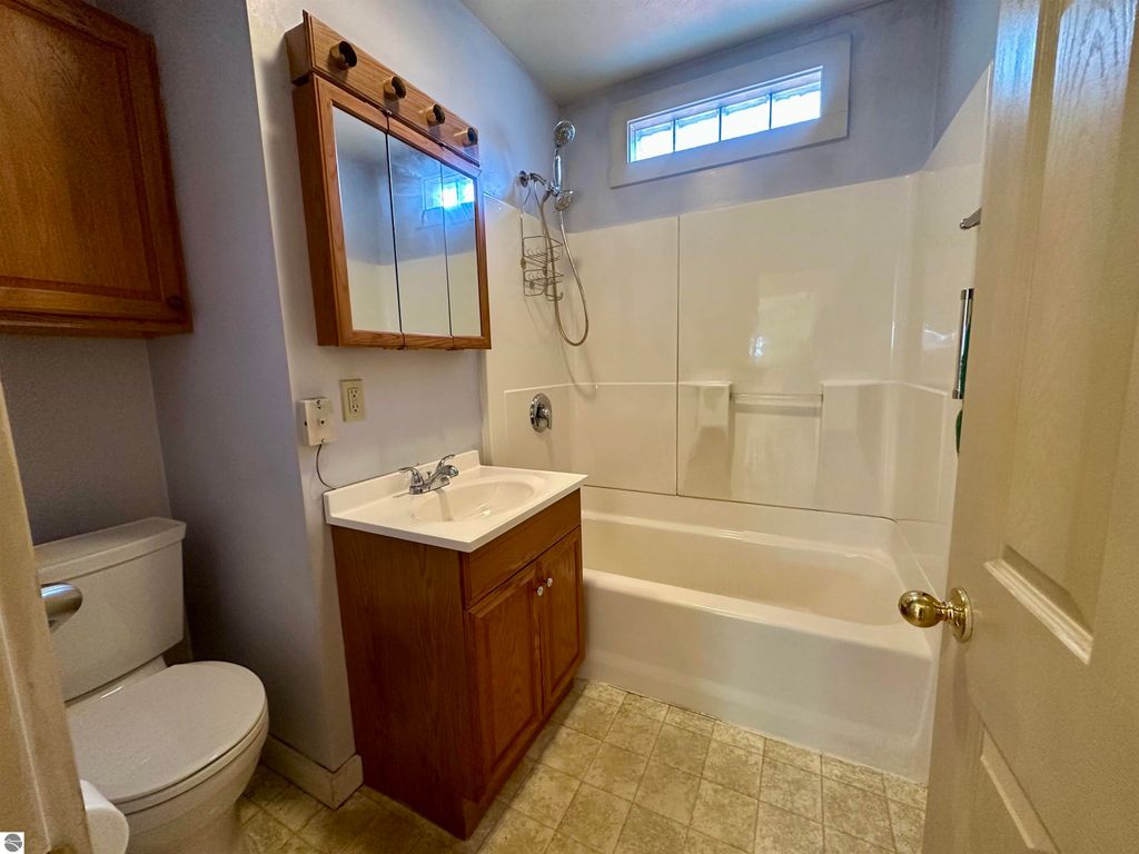 Bathroom with shower-tub combo, wooden cabinet, and mirror, showcasing clean, updated fixtures in a Traverse City bungalow listing.