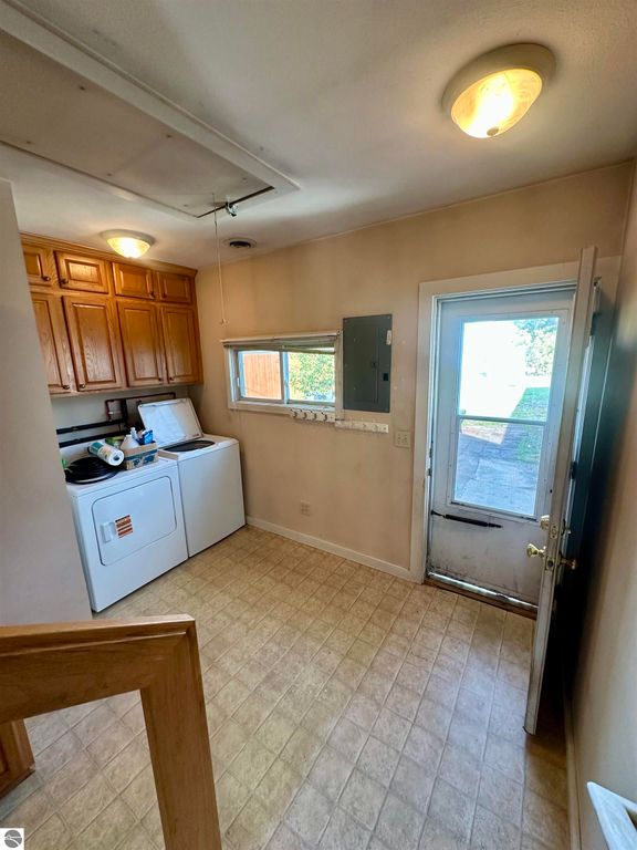Laundry area with washer and dryer, wooden cabinets, door leading to backyard, and window providing natural light, showcasing the functionality of the home at 224 W Fifteenth Street, Traverse City, MI.