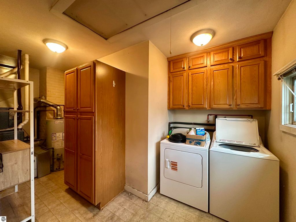 Laundry room featuring a washer and dryer, wooden cabinets, and utility shelving in a cozy bungalow in Traverse City, MI.