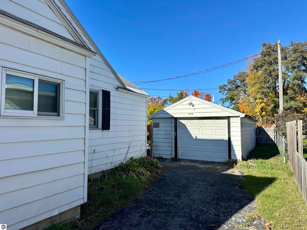 Side view of a bungalow at 224 W Fifteenth Street, Traverse City, featuring a garage, backyard, and clear blue sky, highlighting the property's outdoor space and nearby foliage.