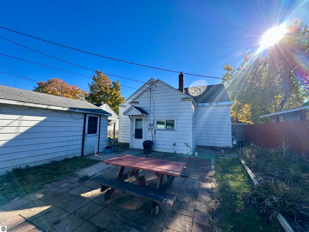 Backyard view of bungalow at 224 W Fifteenth Street, Traverse City, featuring a wooden picnic table, garage, and fenced yard under clear blue sky.