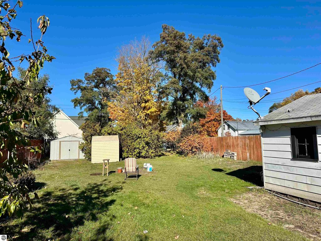 Backyard view of bungalow at 224 W Fifteenth Street, Traverse City, featuring green lawn, shed, chairs, and autumn foliage.
