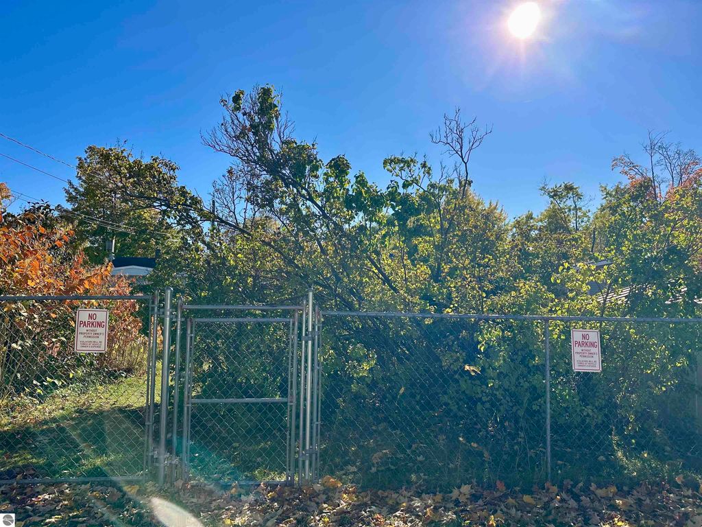 Fenced area with "No Parking" signs, surrounded by lush greenery and trees, in a sunny outdoor setting near 224 W Fifteenth Street, Traverse City, MI.
