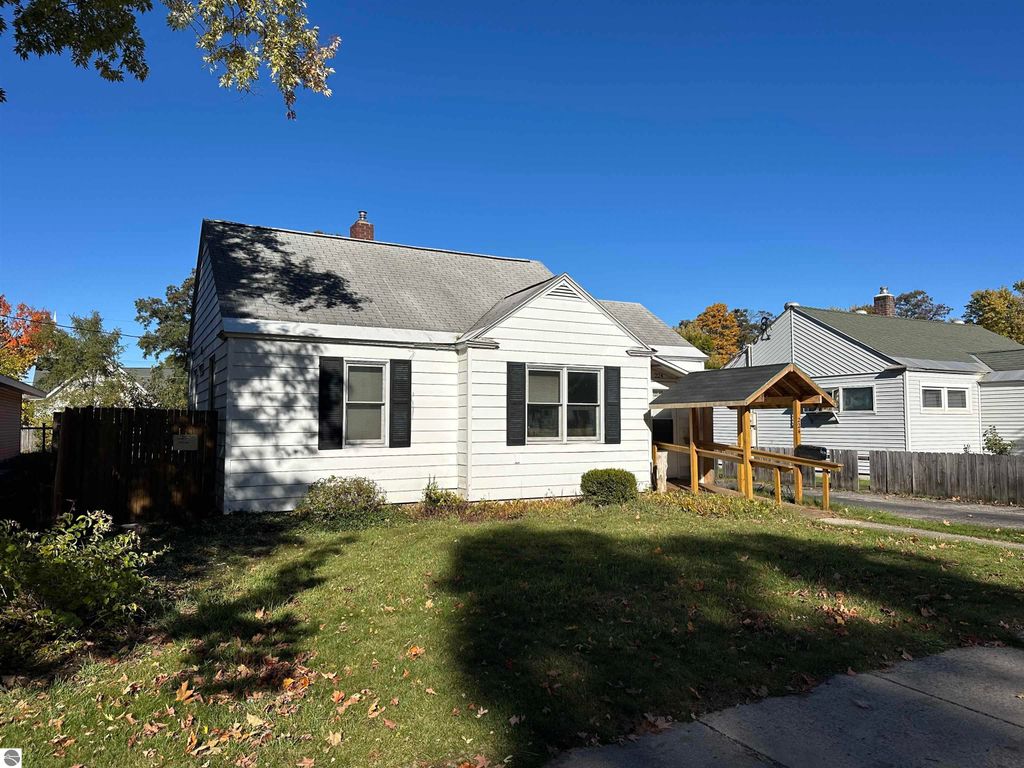 Bungalow exterior at 224 W Fifteenth Street, Traverse City, featuring a fenced yard, porch, and nearby trees in a residential neighborhood.