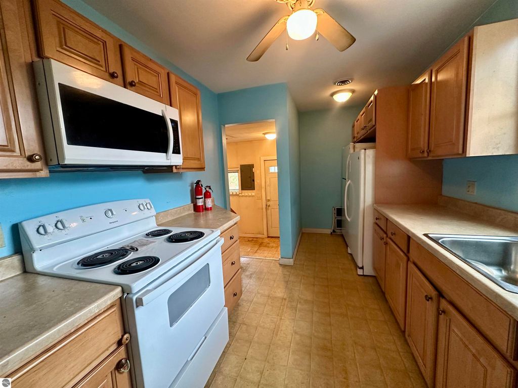 Kitchen featuring modern appliances including a stove, microwave, and refrigerator, with light wood cabinetry and blue walls, in a bungalow located at 224 W Fifteenth Street, Traverse City, MI.