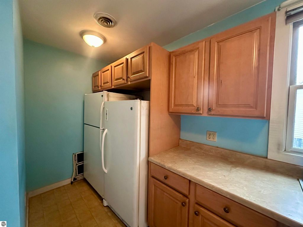 Kitchen area featuring white refrigerator, wooden cabinets, and light blue walls in a bungalow for sale in Traverse City, MI.