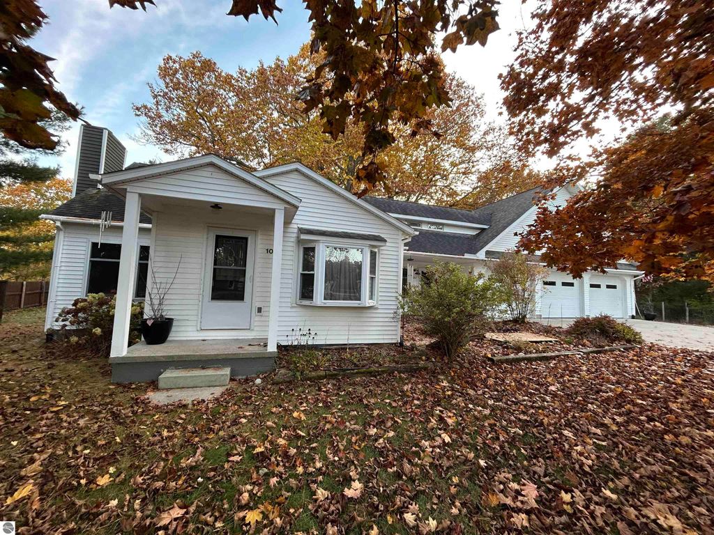 Charming white house at 1007 W First Street, Tawas City, MI, surrounded by autumn leaves and greenery, featuring a welcoming porch and attached garage.