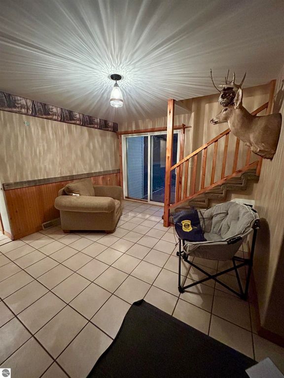Cozy living area with a comfortable couch, sliding glass door, wooden staircase, and a mounted deer head, showcasing a welcoming ambiance in the Tawas City home for sale.
