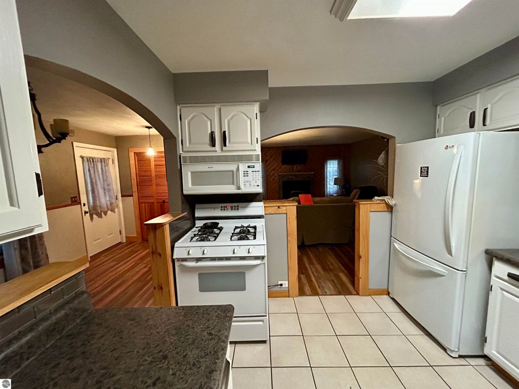 Modern kitchen view featuring a gas stove, white cabinetry, and an open layout connecting to a cozy living area in a home for sale at 1007 W First Street, Tawas City, MI.