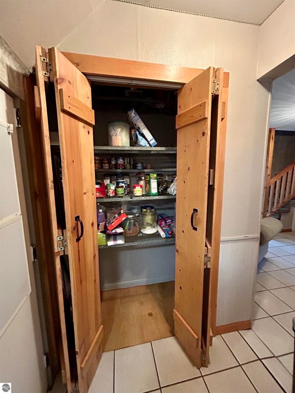 Pantry with wooden double doors open, showcasing shelves filled with various food items and containers, highlighting storage space in the home at 1007 W First Street, Tawas City, MI.