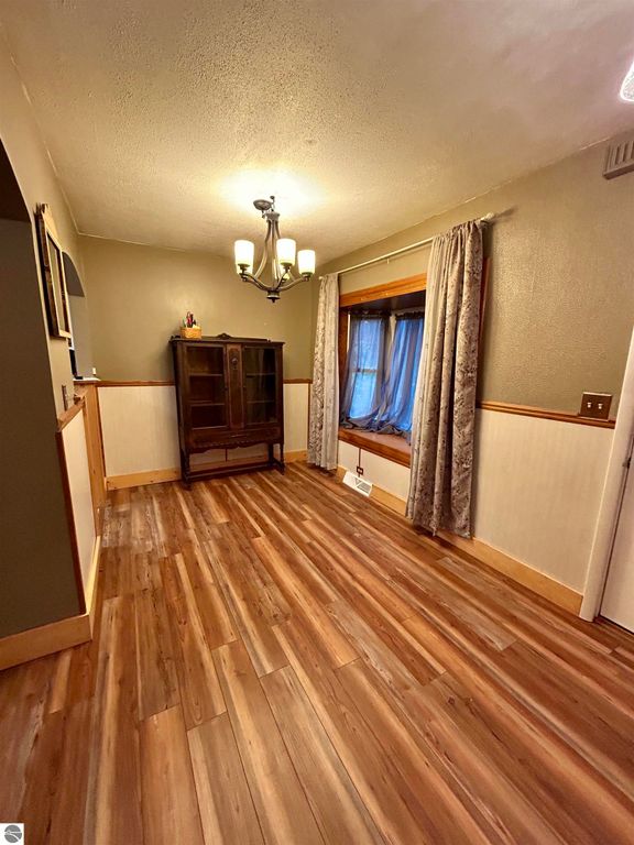 Cozy interior view of a home at 1007 W First Street, Tawas City, featuring wooden flooring, a decorative chandelier, and a window seat with curtains, ideal for families seeking comfort and space.