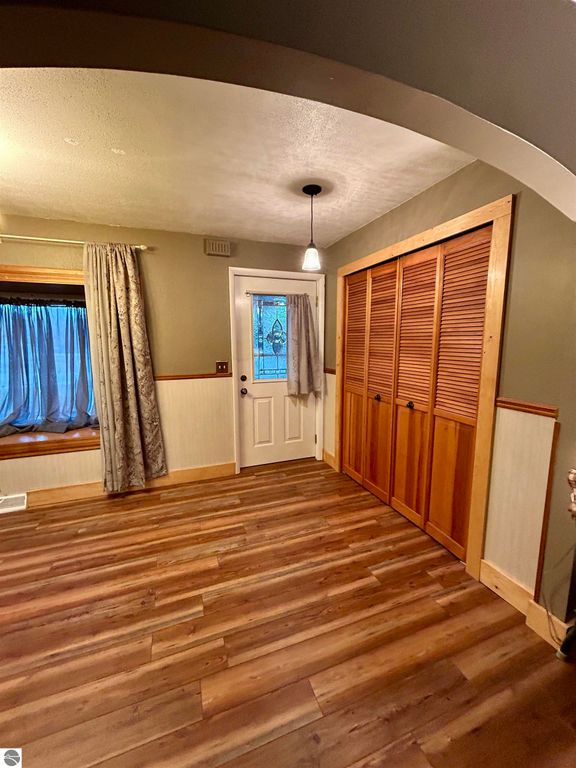 Interior view of a welcoming entryway featuring wooden flooring, a decorative closet, a door with a glass panel, and a window with curtains, ideal for showcasing the cozy ambiance of the home at 1007 W First Street, Tawas City, MI.