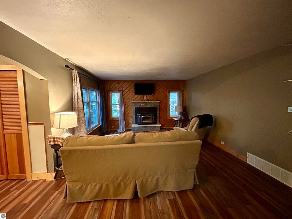 Cozy living room featuring a comfortable sofa, wooden flooring, a fireplace, and large windows, showcasing a warm and inviting atmosphere ideal for family gatherings in the Tawas City home for sale.