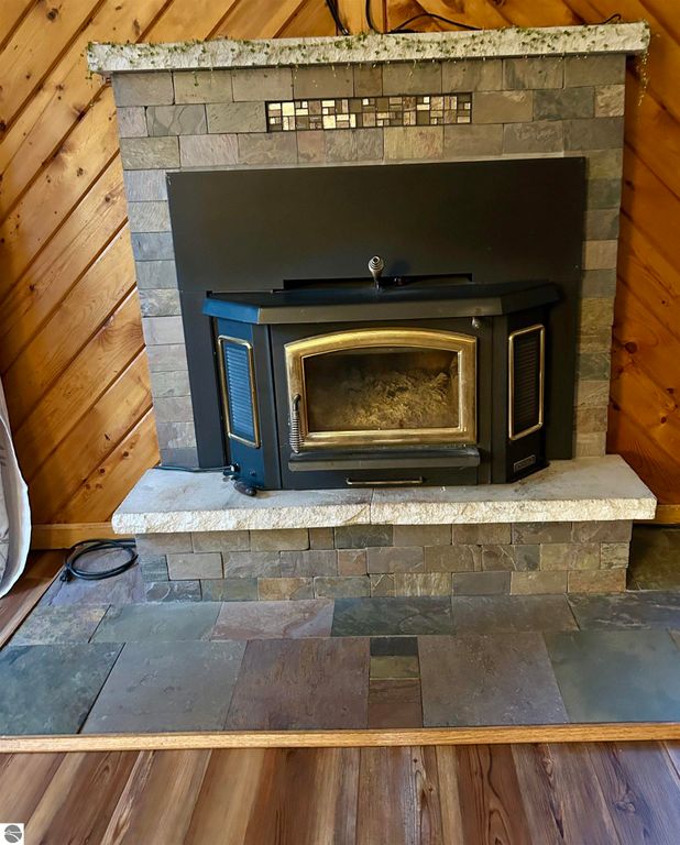 Wood stove with a stone and slate surround, featuring a decorative tile border, set against a wooden wall in a cozy living space.