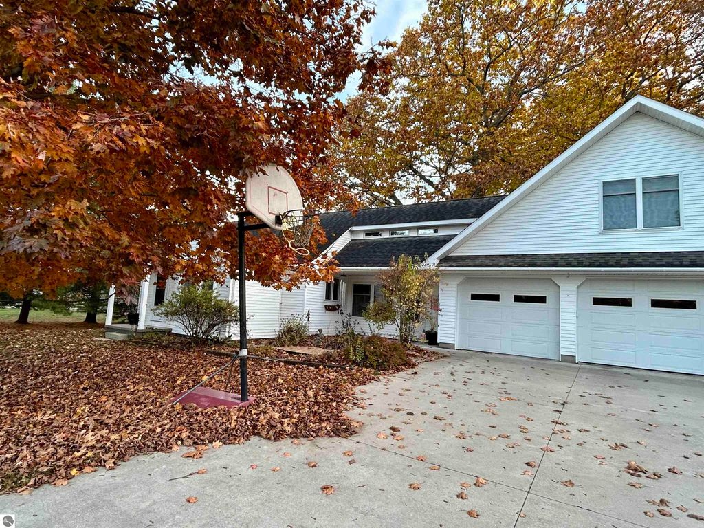 Basketball hoop in front of a white house surrounded by autumn leaves, highlighting the property's outdoor space at 1007 W First Street, Tawas City, MI.