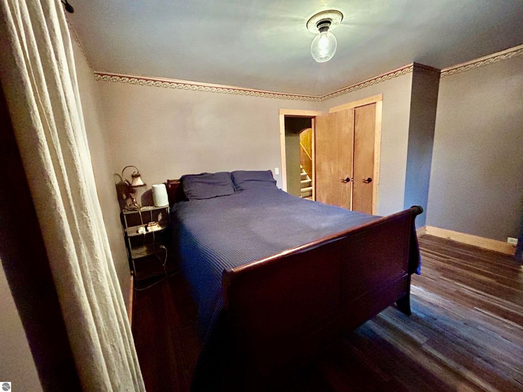 Cozy bedroom featuring a wooden bed with blue bedding, nightstand with lamp, and decorative wall trim, showcasing the inviting interior of the home at 1007 W First Street, Tawas City, MI.
