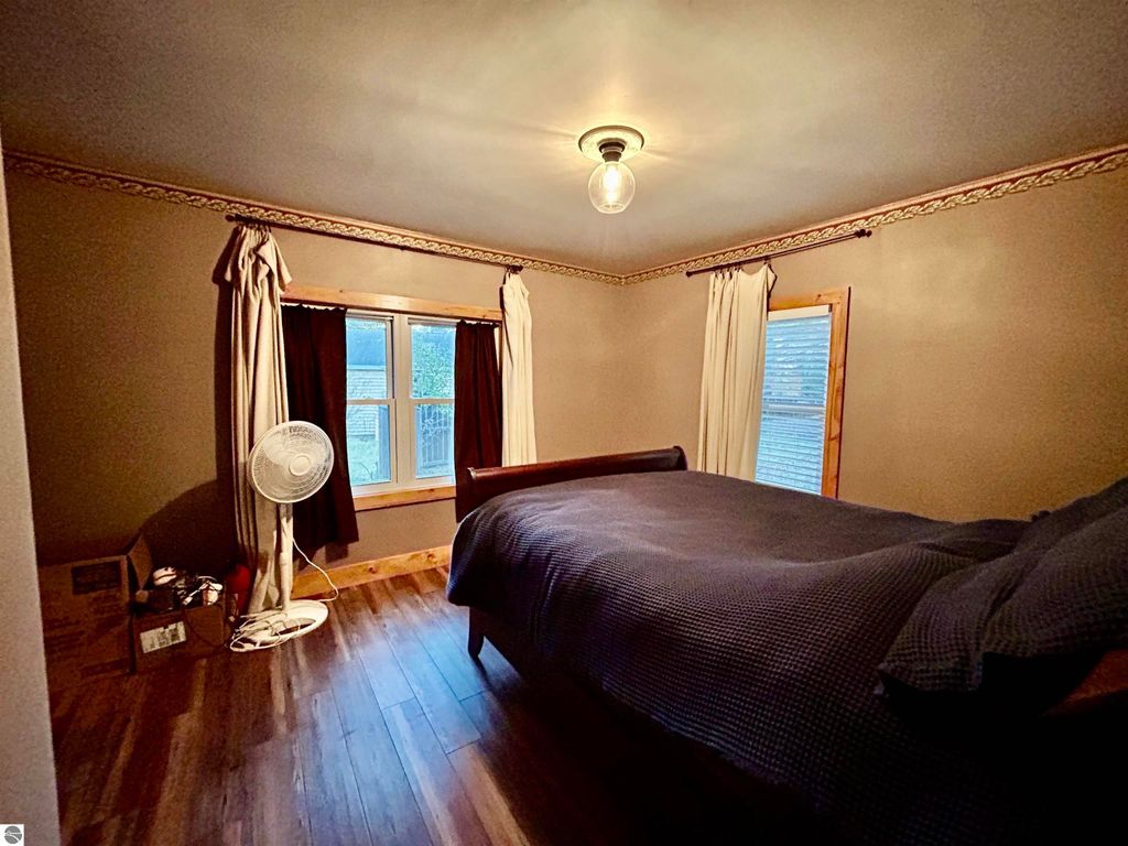 Cozy bedroom featuring a bed, large windows with curtains, wooden flooring, and a ceiling light, showcasing a serene atmosphere in the home at 1007 W First Street, Tawas City, MI.