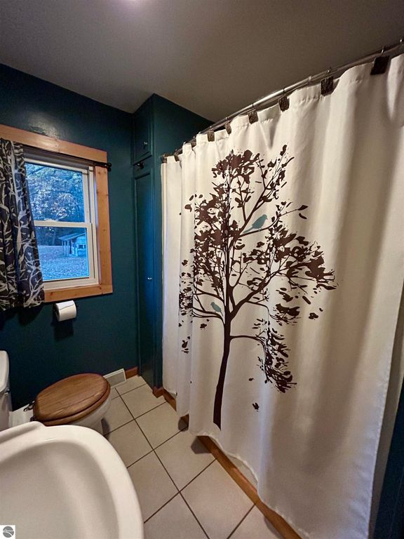 Bathroom featuring a decorative tree-patterned shower curtain, wooden toilet seat, and green walls, capturing a cozy and serene atmosphere.