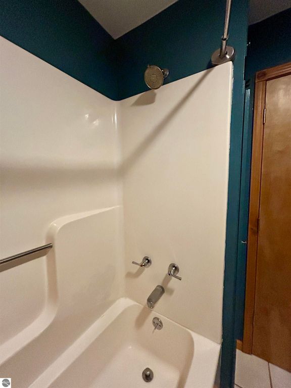 Shower with a white tub and modern fixtures, featuring a teal wall and wooden door, showcasing the bathroom's design in the Tawas City home listing.