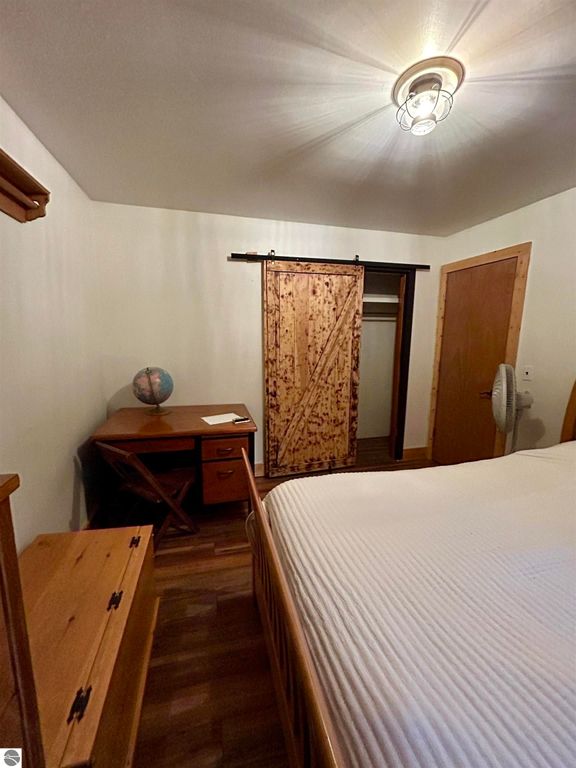 Cozy bedroom featuring a wooden bed, desk with a globe, and sliding barn door leading to a closet, showcasing a warm and inviting atmosphere suitable for a family home in Tawas City, MI.