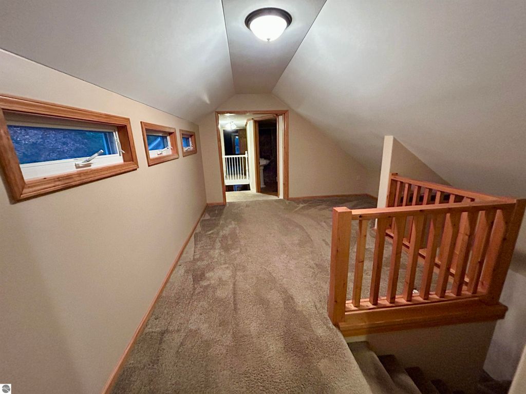 Upper hallway of a home at 1007 W First Street, Tawas City, featuring carpeted flooring, wooden railings, and multiple windows providing natural light, ideal for family living.