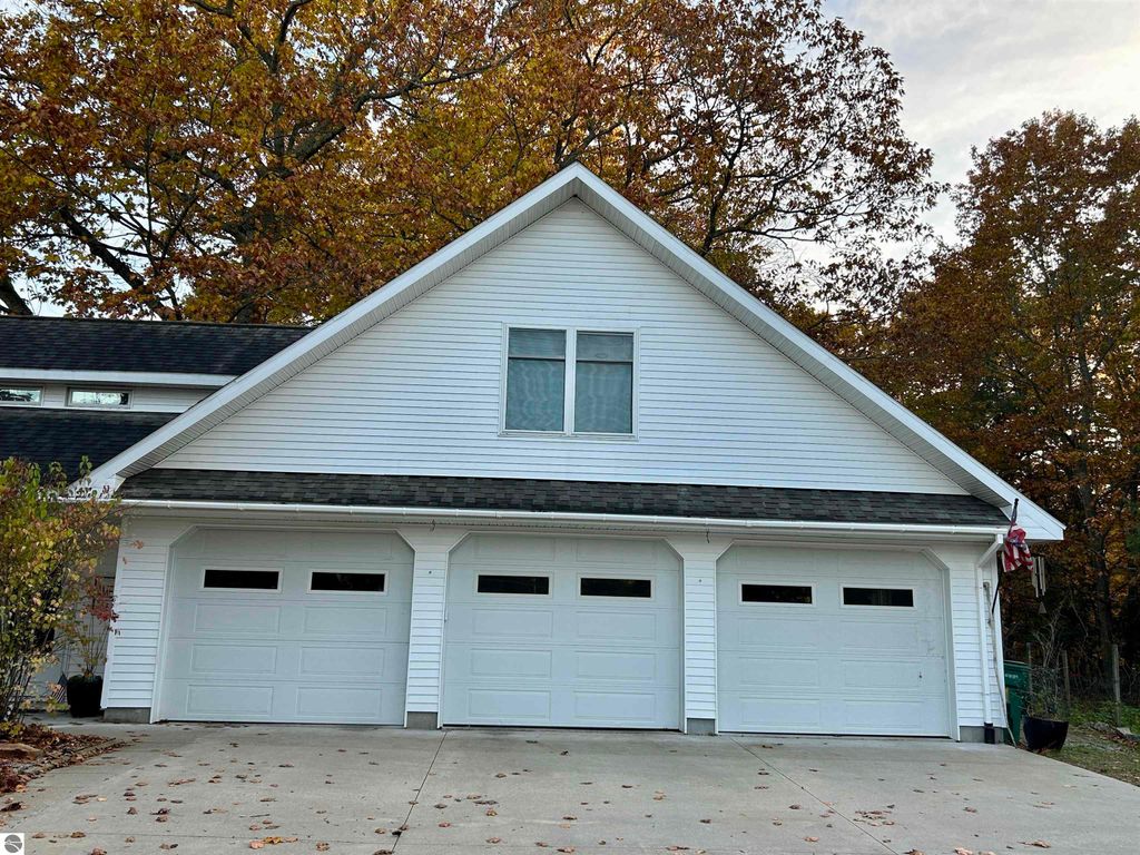 Garage with three doors and a peaked roof, surrounded by autumn foliage, located at 1007 W First Street, Tawas City, MI, emphasizing ample storage space for hobbies and outdoor activities.