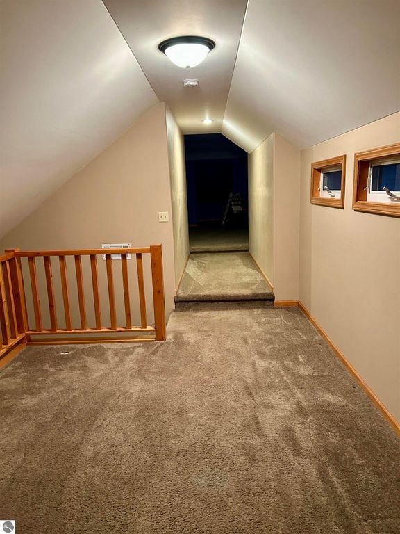 Hallway with carpet flooring and wooden railing, featuring a light fixture and windows, leading to an open space in a residential property at 1007 W First Street, Tawas City, MI.
