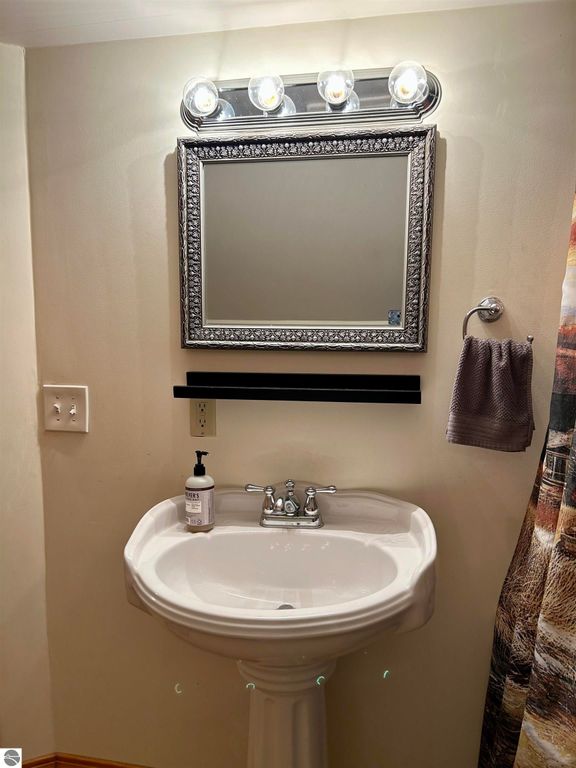 Bathroom sink with ornate mirror, wall-mounted lighting, and hand towel, highlighting the home's interior features at 1007 W First Street, Tawas City, MI.