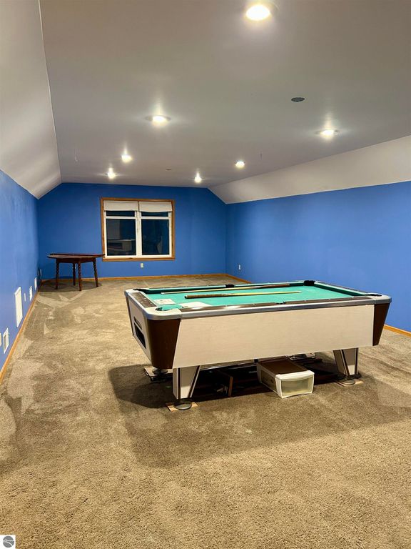 Expansive bonus room with billiards table, blue walls, and natural light from window, ideal for family entertainment in Tawas City home listing.