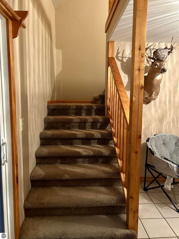 Staircase leading to upper level with wooden railing, featuring a deer mount on the wall, showcasing the cozy interior of the home at 1007 W First Street, Tawas City, MI.