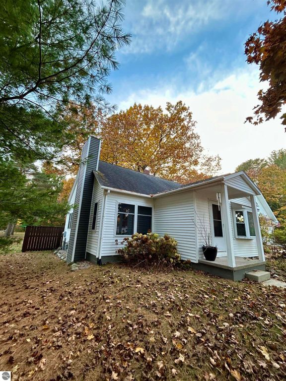 Charming white home at 1007 W First Street, Tawas City, surrounded by autumn foliage, showcasing a welcoming porch and spacious yard.