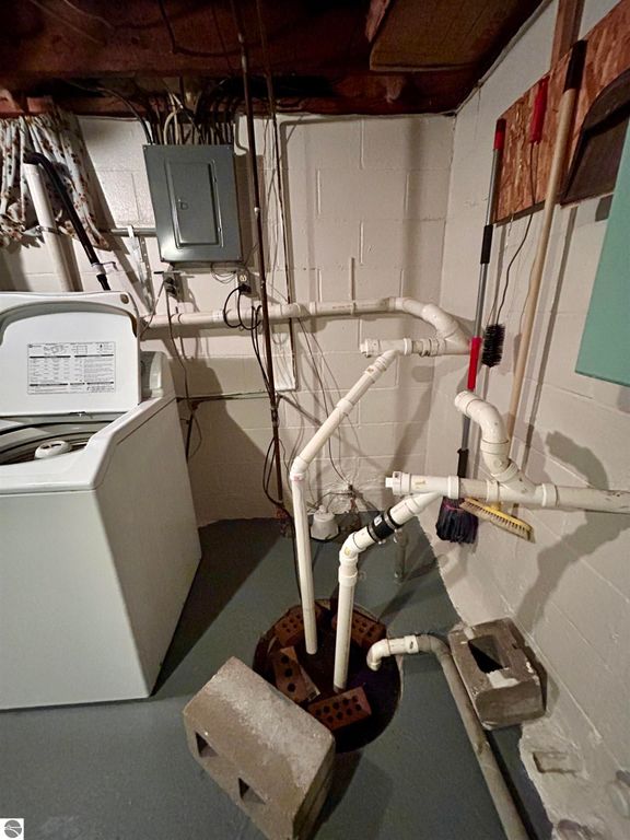 Basement utility area featuring a washing machine, plumbing pipes, and drainage system, illustrating functional aspects of the home at 1007 W First Street, Tawas City, MI.
