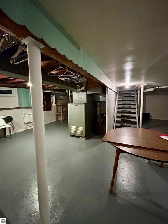 Basement interior of a home at 1007 W First Street, Tawas City, featuring a table, storage areas, and a staircase, emphasizing potential for extra living space.