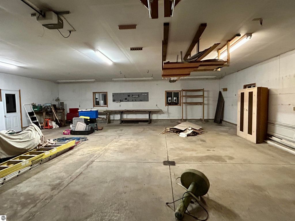 Spacious garage interior with concrete flooring, overhead lighting, and various storage items, showcasing ample space for hobbies and storage at 1007 W First Street, Tawas City, MI.