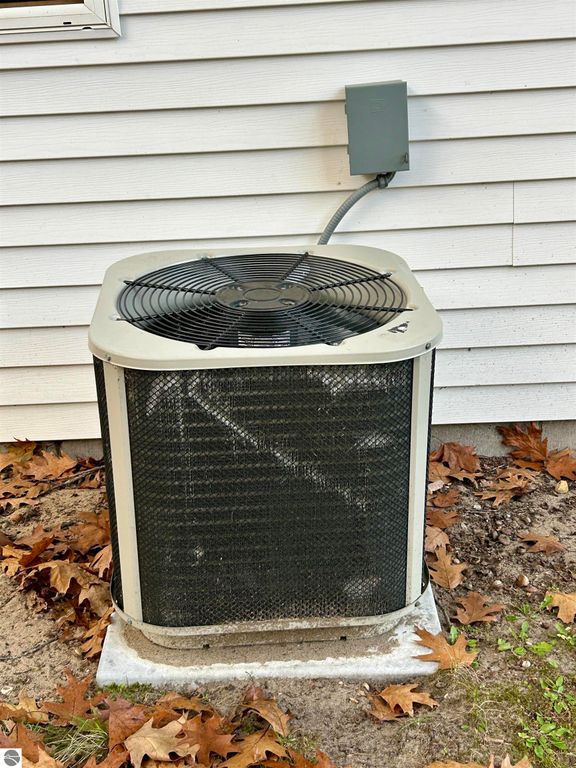 Air conditioning unit installed outside a residential home, surrounded by fallen leaves and adjacent to a white house wall.
