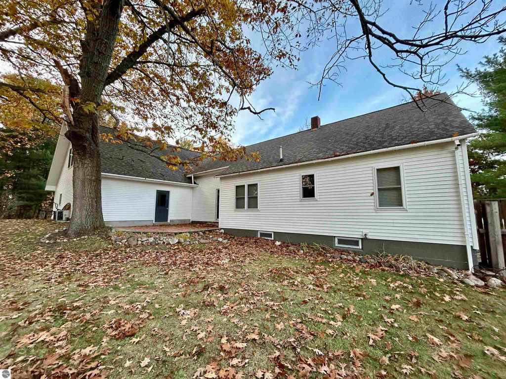 Exterior view of a residential home at 1007 W First Street, Tawas City, MI, showcasing a white siding structure surrounded by autumn leaves and trees, emphasizing a tranquil park-like setting ideal for families.