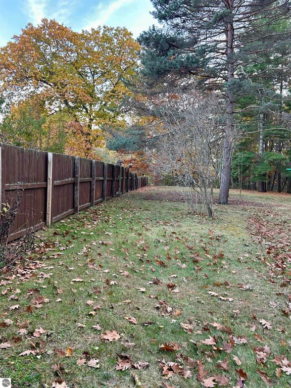 Fenced backyard with autumn foliage, featuring a grassy area and scattered fallen leaves, enhancing the tranquil setting of the property at 1007 W First Street, Tawas City, MI.
