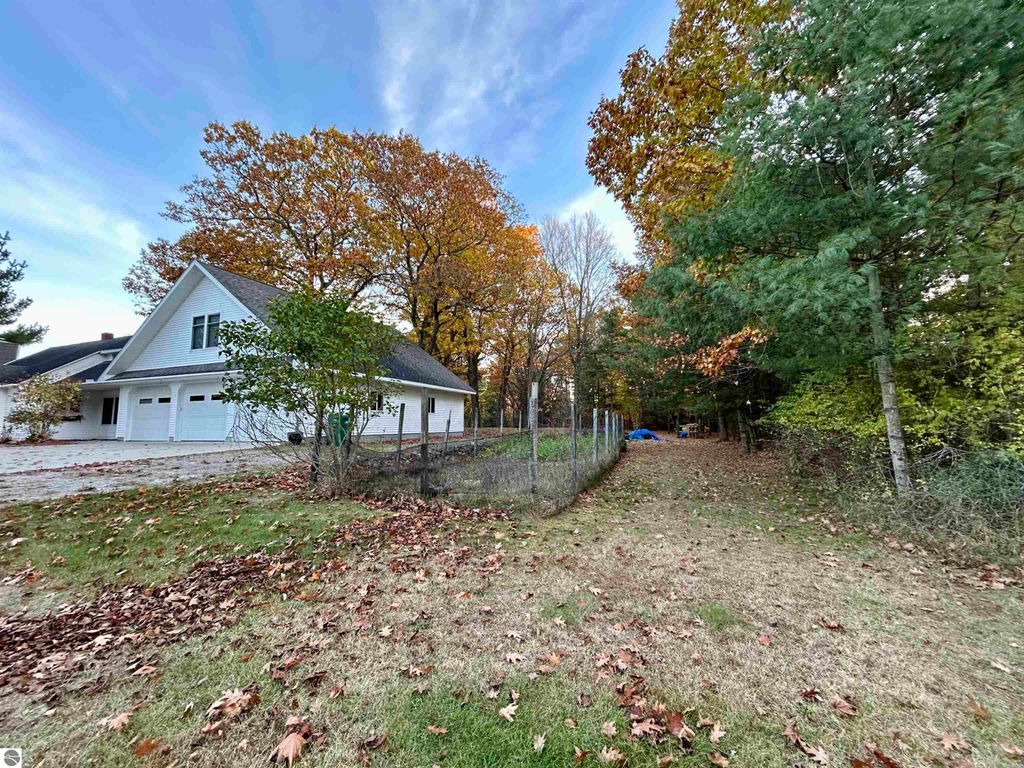 Residential property at 1007 W First Street, Tawas City, MI, featuring a spacious yard with autumn foliage, adjacent to a fenced area and trees, highlighting a peaceful, park-like setting ideal for families.
