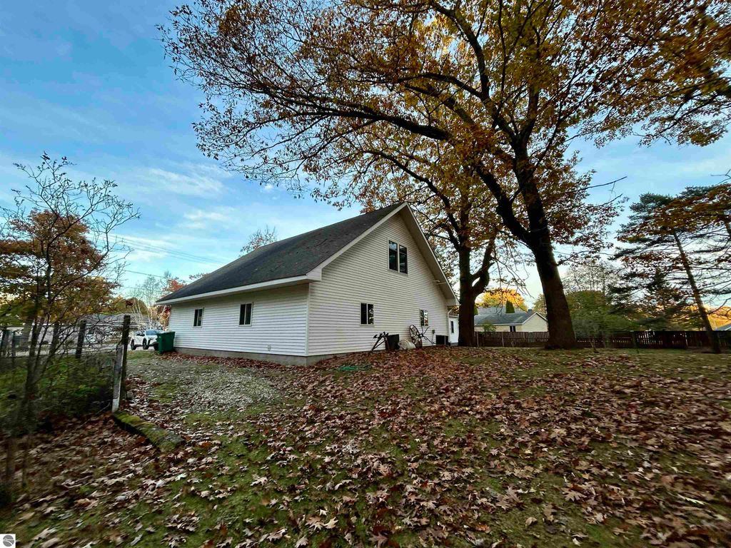 White residential home surrounded by autumn leaves and trees, located at 1007 W First Street, Tawas City, MI, showcasing a serene park-like setting ideal for families.