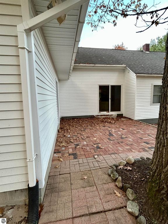 Patio area of a residential home featuring brick pavers, surrounded by leaves and a tree, with a view of sliding glass doors leading into the house, showcasing the outdoor space of the property at 1007 W First Street, Tawas City, MI.
