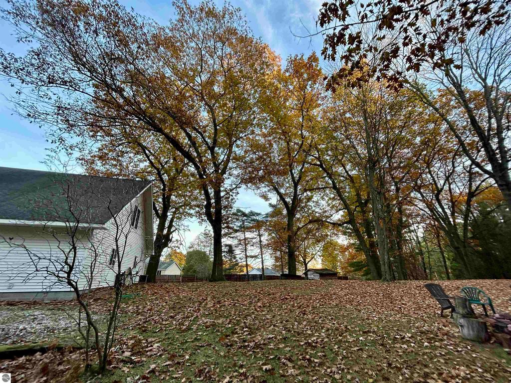 Backyard view of a residential property at 1007 W First Street, Tawas City, MI, featuring autumn foliage, fallen leaves, and a peaceful, park-like setting with trees and seating area.