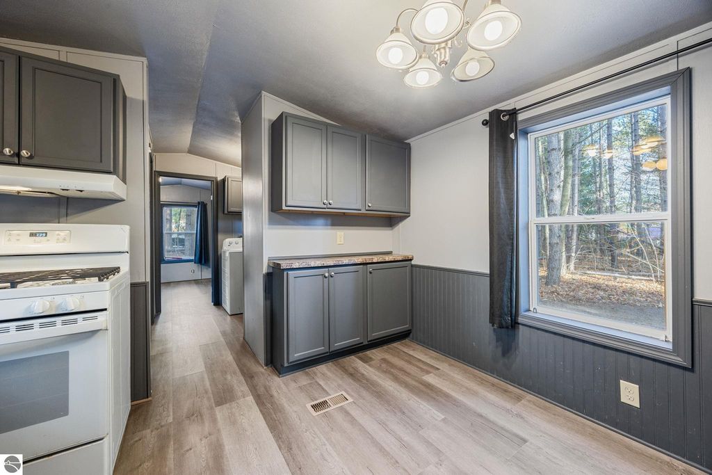 Modern kitchen interior featuring gray cabinets, gas stove, and large window overlooking wooded area, highlighting the move-in ready condition of the 3-bedroom home at 8401 Independence Avenue, Cadillac, MI.