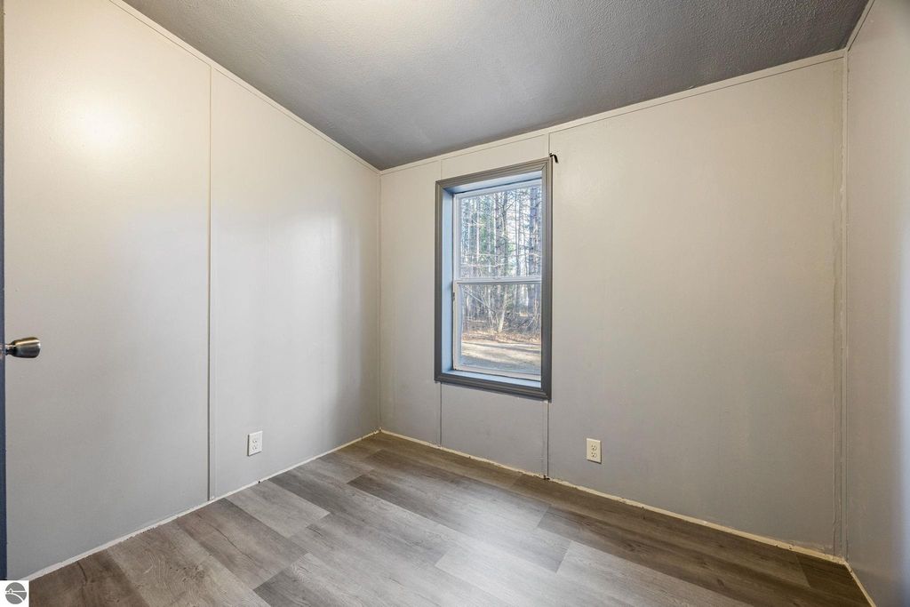 Interior view of a freshly painted bedroom with new flooring, featuring a window overlooking a wooded area, part of a 3-bedroom home for sale at 8401 Independence Avenue, Cadillac, MI.