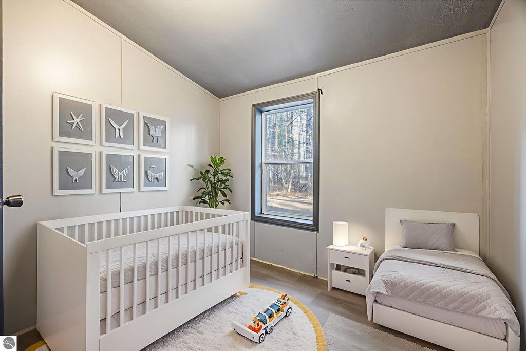 Cozy children's bedroom featuring a white crib, single bed, decorative wall art, and a window with a view of trees, designed for a move-in ready home at 8401 Independence Avenue, Cadillac, MI.