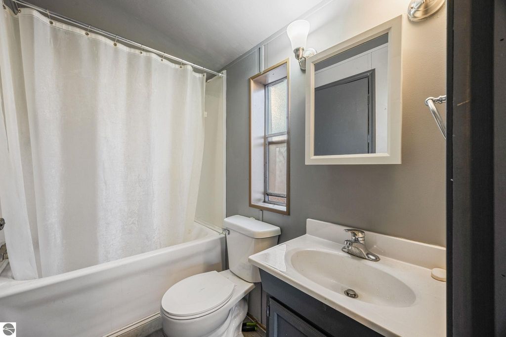 Bathroom with shower curtain, toilet, sink, and window, featuring modern fixtures and neutral colors, highlighting the updated interior of the 3-bedroom home for sale at 8401 Independence Avenue, Cadillac, MI.