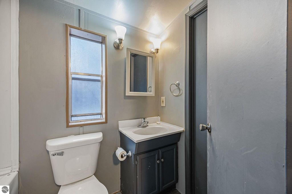 Bathroom interior featuring a white toilet, dark cabinetry with sink, mirror, and window, showcasing a clean and updated space in a 3-bedroom home for sale at 8401 Independence Avenue, Cadillac, MI.