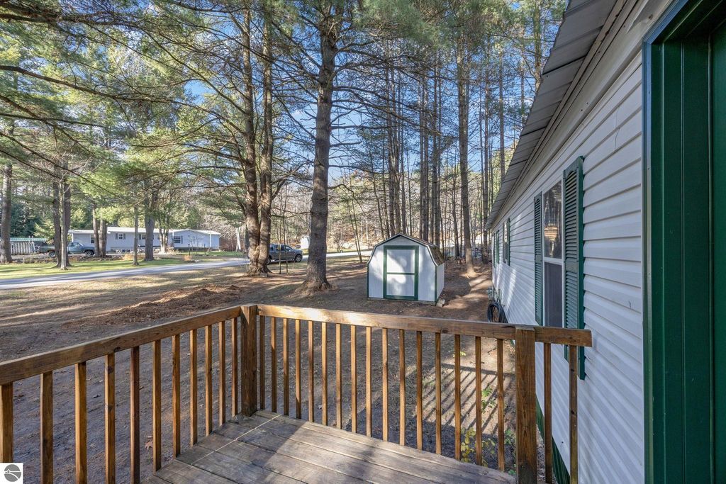 View from the porch of a 3-bedroom home at 8401 Independence Avenue, Cadillac, MI, featuring a wooden railing, nearby storage shed, and surrounding trees, highlighting the property's spacious lot and serene setting.