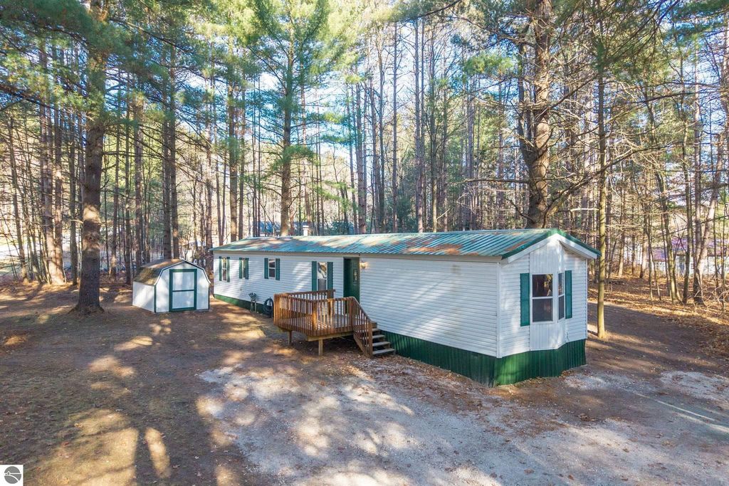 3-bedroom, 1-bathroom home with green metal roof, wooden deck, and storage shed, surrounded by tall trees on large lot in Cadillac, MI.