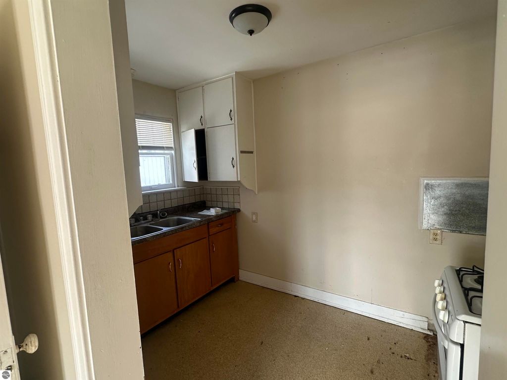 Cozy kitchen interior with wooden cabinets, sink, and gas stove, showcasing the charm of the 2-bedroom home for sale at 110 W State Street, Clare, MI.